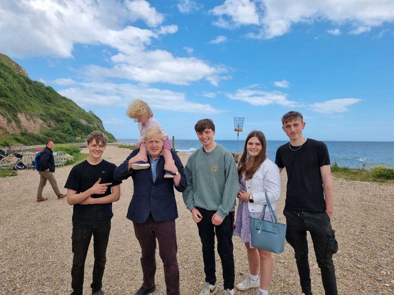 Boris Johnson carries son Wilfred, 4, on his shoulders as they pose with locals during seaside stroll