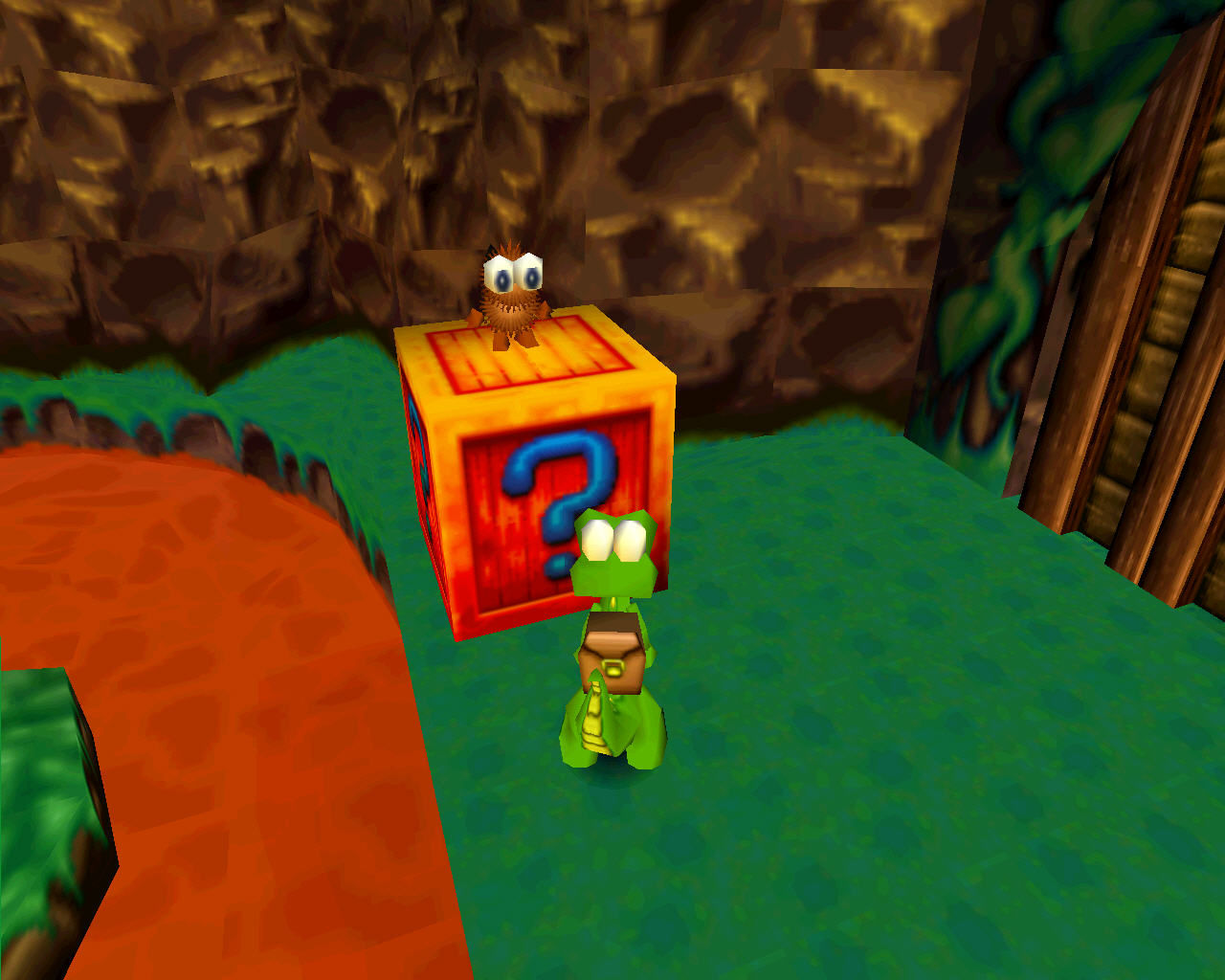 A small upright crocodile in a backpack stands in front of a box with a furry gobbo on top. Croc: Legend of the Gobbos - Argonaut Games