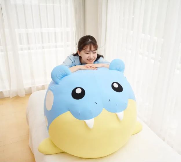 A woman rests her hands on the head of a life-size Spheal plush gazing adoringly