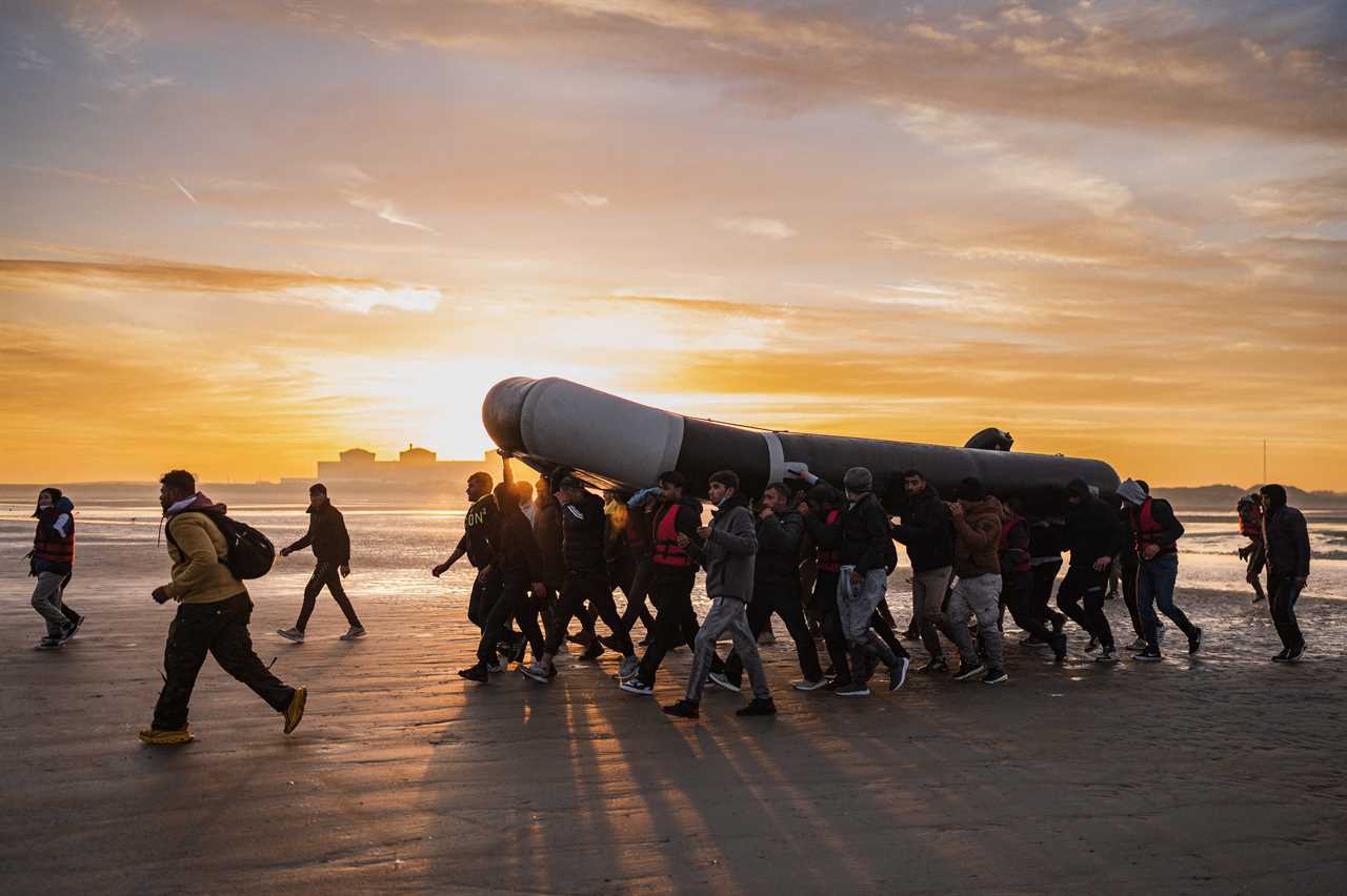 -- AFP PICTURES OF THE YEAR 2022 -- Migrants carry a smuggling boat on their shoulders as they prepare to embark on the beach of Gravelines, near Dunkirk, northern France on October 12, 2022, in a attempt to cross the English Channel. (Photo by Sameer Al-DOUMY / AFP) / AFP PICTURES OF THE YEAR 2022 (Photo by SAMEER AL-DOUMY/AFP via Getty Images)