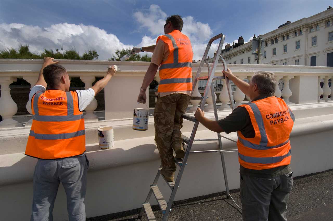 BCD2X0 Convicted criminals doing painting and decorating in orange tabards with community payback slogan on the back